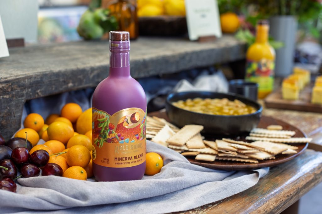 Minerva Olive Oil in a purple bottle with citrus and crackers.